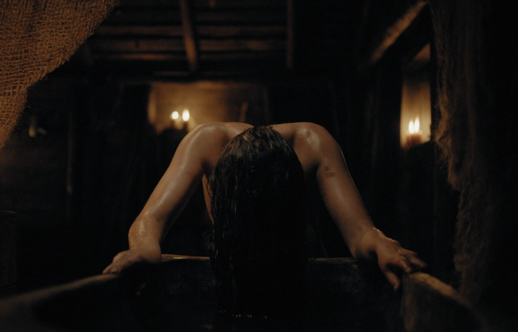 A beautiful woman lies over a bath with a rustic interior behind her