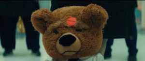 A sad looking teddy bear with a "defective" sticker on his head