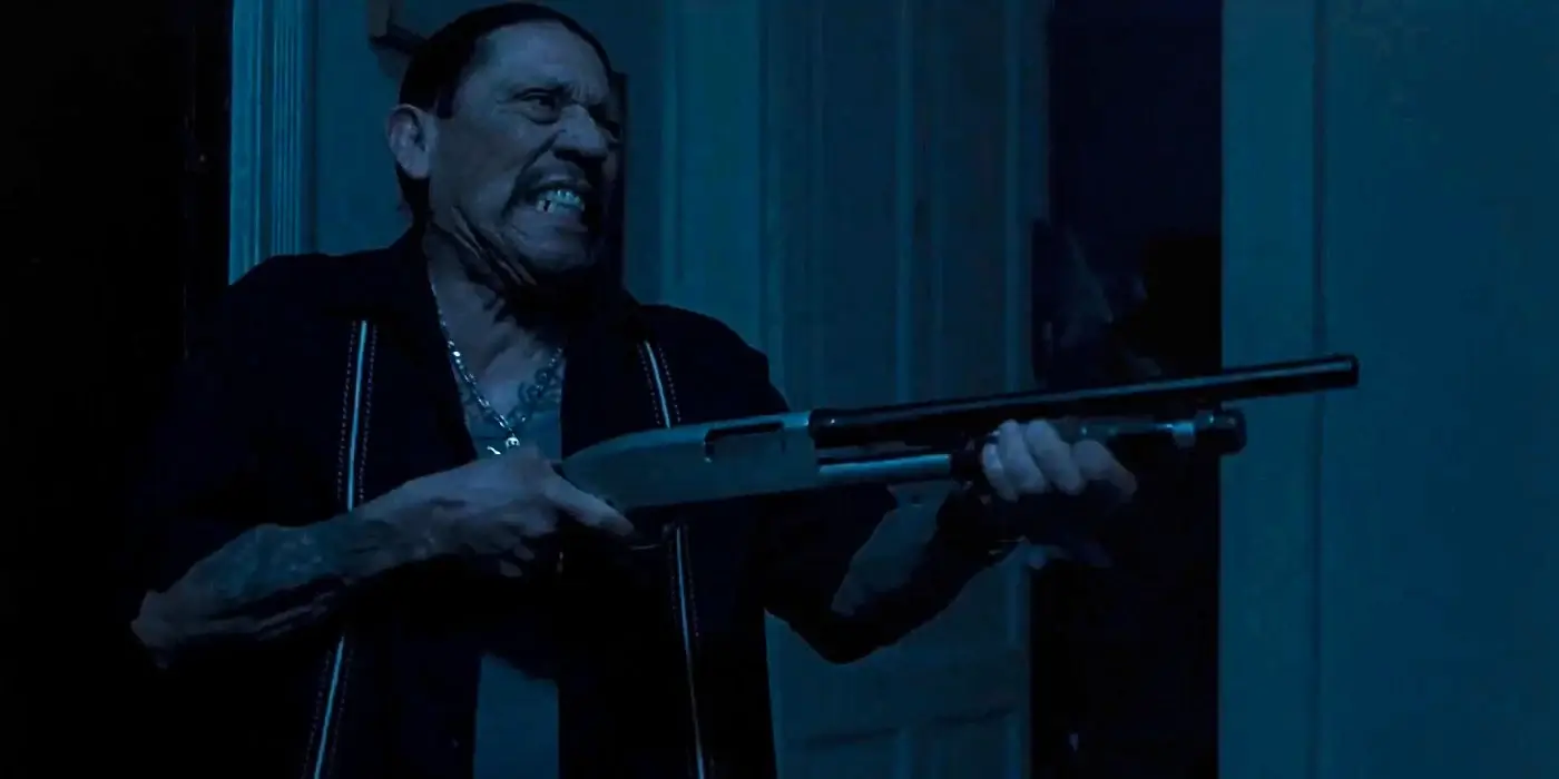 Danny Trejo holding a shotgun in a dark hallway with an open door behind him