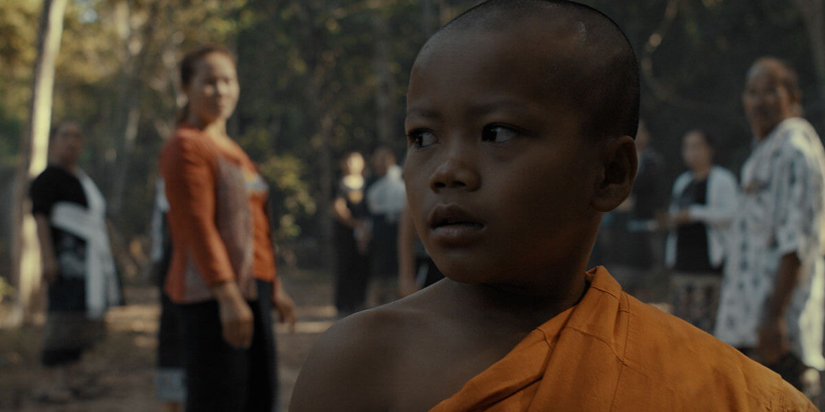 A young Lao boy wearing ceremonial robes with people in the background