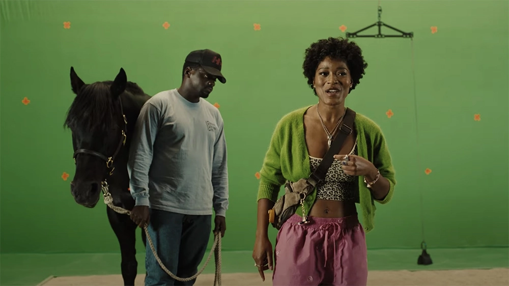 Daniel Kaluuya and Keke Palmer as their characters in Nope stand in front of a green screen with a black horse 
